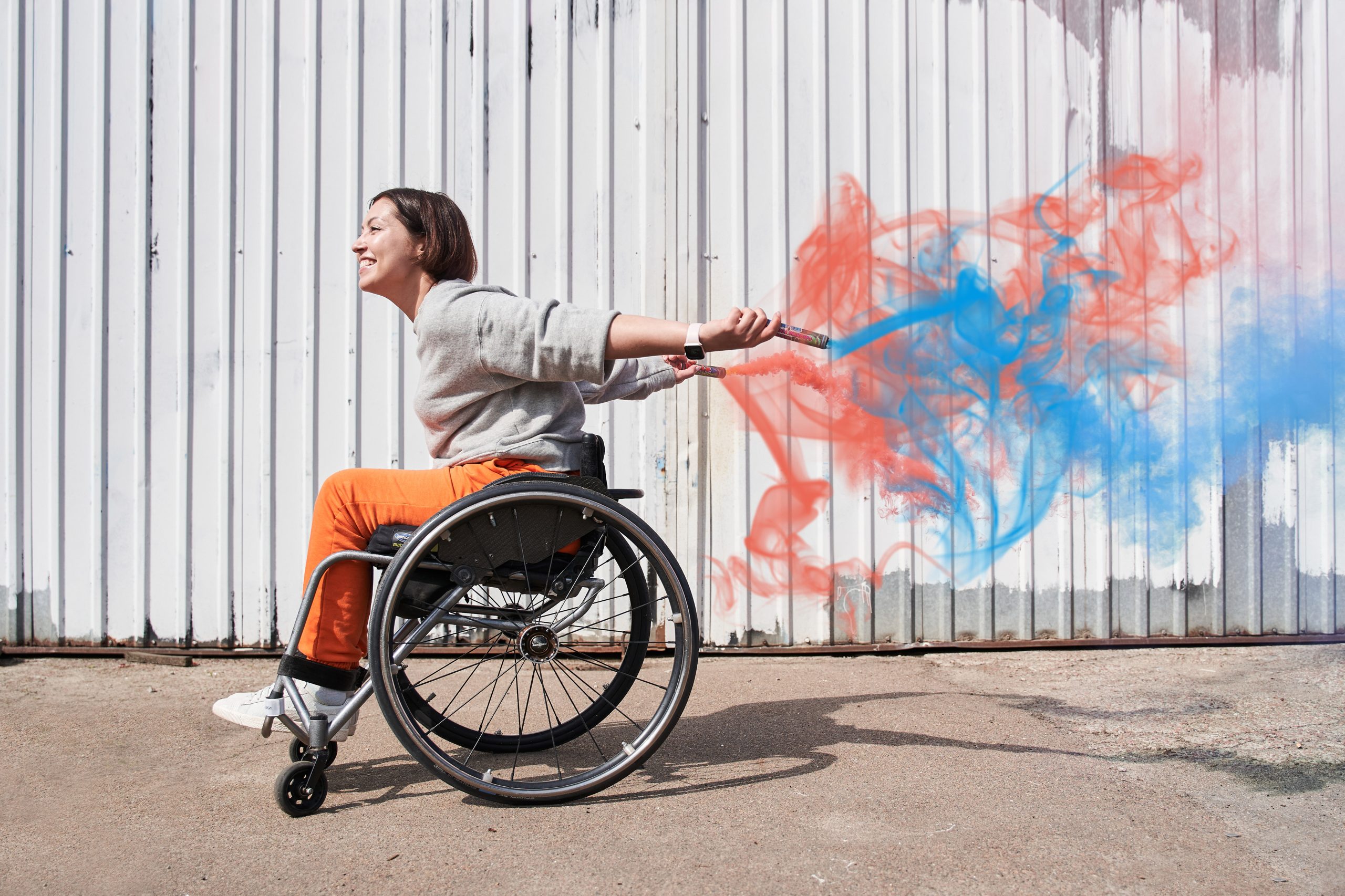 Junge Frau im Rollstuhl hält zwei bunte Rauchfackeln