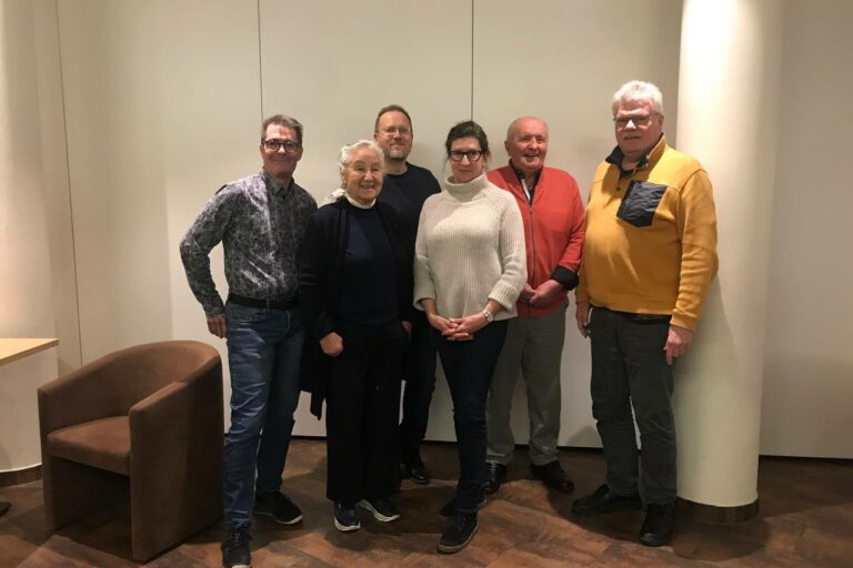 Die Vorstandsmitglieder haben sich vor einer hellen Wand nebeneinander zum Gruppenfoto aufgestellt und lächeln in die Kamera.