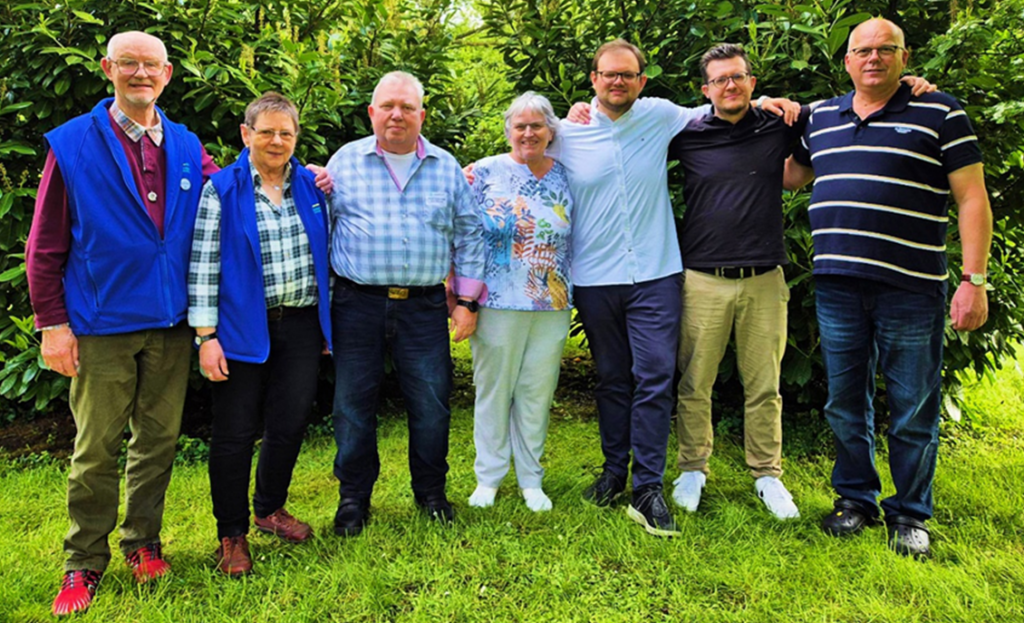 Sieben Vorstandsmitglieder des CIV NRW haben sich auf dem Rasen vor ein paar Bäumen zum Gruppenfoto in einer Reihe aufgestellt, haben sich die Arme gegenseitig über die Schultern gelegt und lächeln in die Kamera.
