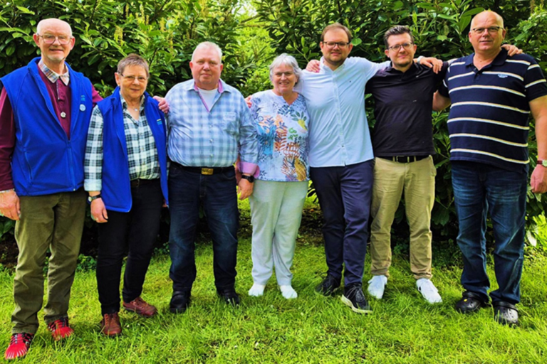 Sieben Vorstandsmitglieder des CIV NRW haben sich auf dem Rasen vor ein paar Bäumen zum Gruppenfoto in einer Reihe aufgestellt, haben sich die Arme gegenseitig über die Schultern gelegt und lächeln in die Kamera.