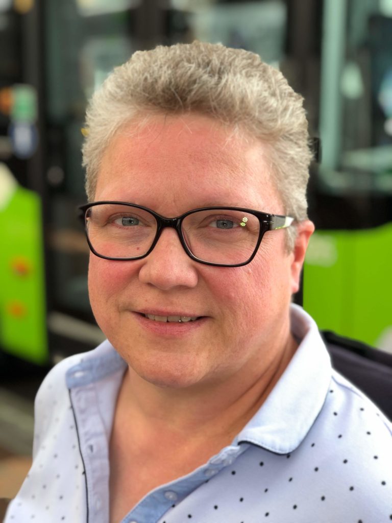Porträtfoto von Annette Runte: Sie hat kurze, graue Haare trägt eine markante Brille mit schwarzem Rahmen und ein hellblaues Hemd mit Kragen und kleinen blauen Punkten. Ihr Blick ist offen, sie lächelt.