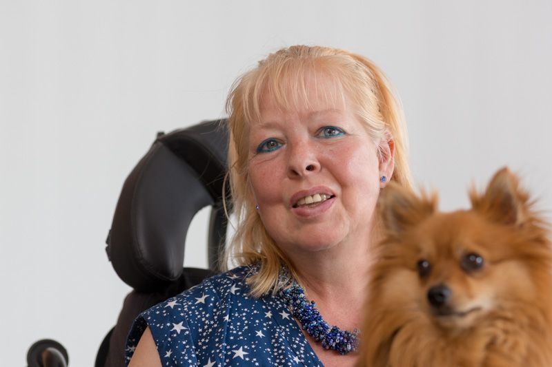Maggy Heggen blickt lächelnd in die Kamera. Auf ihrem Schoß sitzt ein kleiner Hund mit